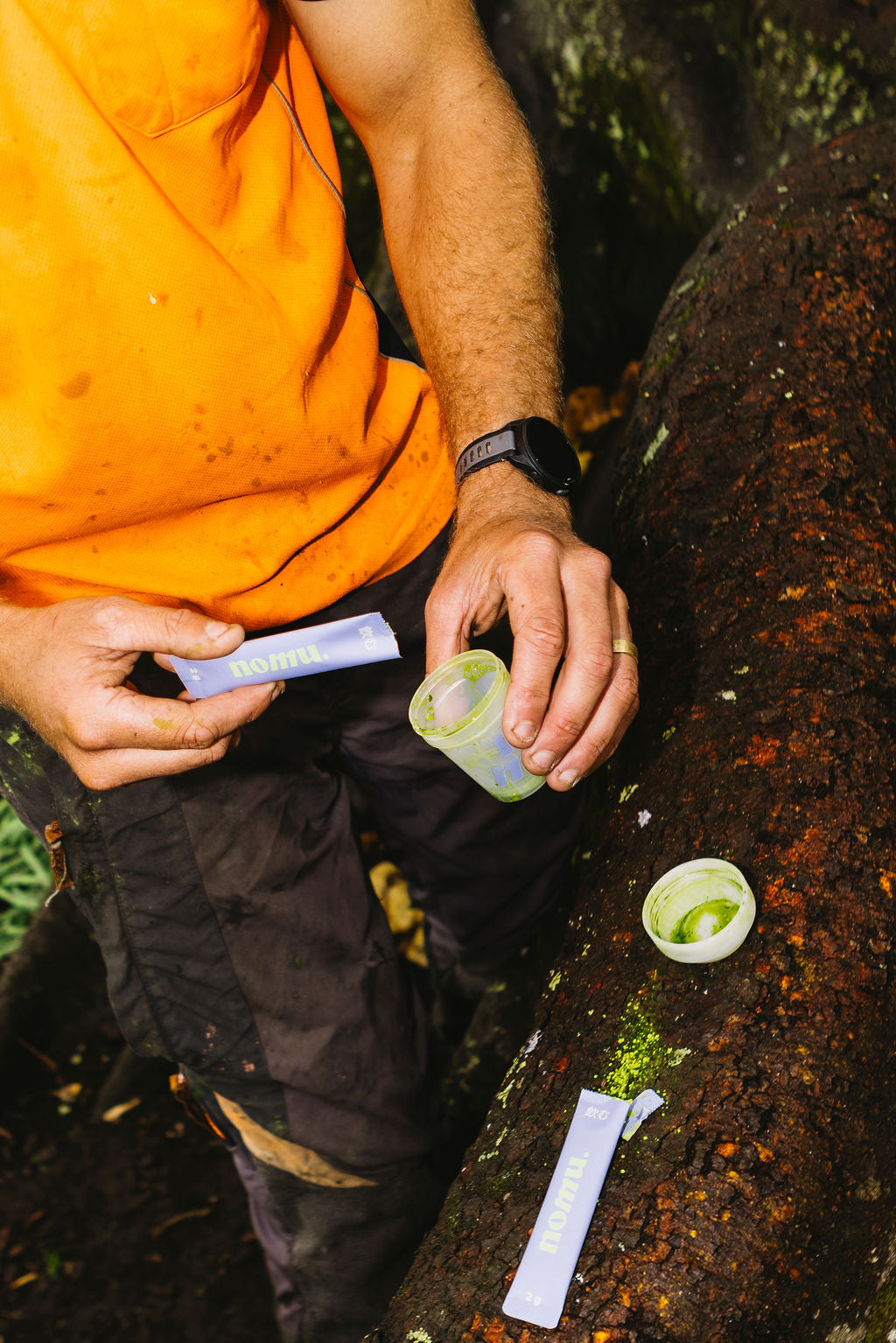 Person outdoors holding a small container and a green object on a rocky surface